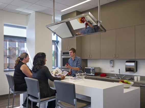 A person cooking a meal in a kitchen while two people sit at the island.