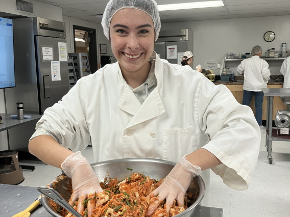 A student wearing a lab coat working with a large bowl of kimchi.