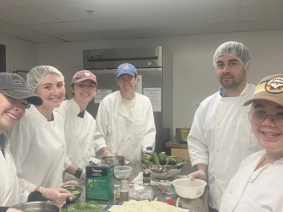 A group of students in lab coats around a table full of food ingredients.